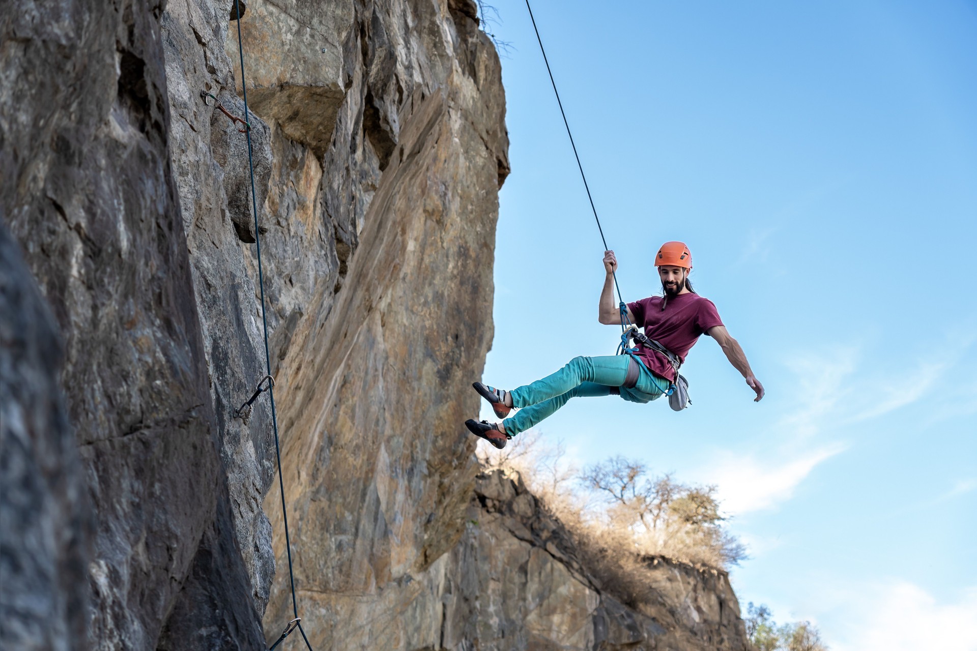 Young man climbing a challenging route on a cliff with a rope.